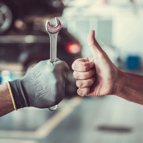 Nahaufnahme der Hände zweier Männer in einer Autowerkstatt - einer mit Daumenhoch-Geste, einer mit Schraubenschlüssel analog nach oben gerichtet.